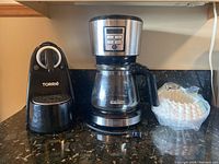Photo showing TORRIE single-serve coffee maker, BLACK+DECKER drip coffee maker, and wrapped coffee filters on countertop.