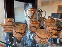 Full view of the porcelain espresso set showing six cups stacked on saucers, coffee pot, creamer, and sugar bowl with heavy decorative artwork and gold accents.