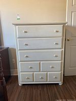 Front view showing 7 drawers with wooden knobs and white laminated finish