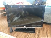 Front view of the LG television showing screen, bezel, stand, and remote placed on surface in front.