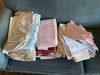 Full view of the assortment of folded linens on couch including floral tablecloth, pink napkins, and other cloths