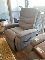 Front-side view of gray fabric upholstered massaging recliner chair showing padded segmented backrest, arms, and attached side pocket with remote control.