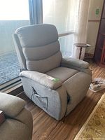 Gray fabric recliner chair angled from front right side, showing padded segmented backrest, armrests, and side pocket with wire loop.