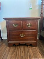 Front view showing the three drawers with brass handles and the base detailing of one wooden night stand.