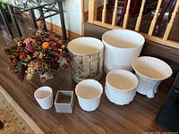 Two large plastic planters, five ceramic planters, and a faux fruit arrangement set on the floor by railing.