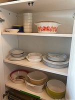 Cupboard shelf showing mix of glass and ceramic dishes including the Pyrex Friendship casserole dish, mixing bowls, and plates.