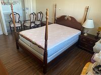 Side angle showing bed frame's wood posts, mattress, and three upholstered chairs behind