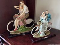 Both poly-resin romantic couple statues on bicycles, one with man and woman in casual attire, one with bride and groom in wedding attire