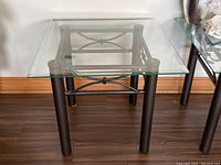 Front view of the square glass top table with matte black metal frame and decorative design on the base.