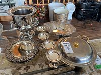 Photo showing silver plated ice bucket, four silver plated champagne glasses, and multiple metal serving dishes on a table.