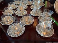 Overview photo showing 12 glass tea cups set in ornate silver plated holders with matching silver plated saucers arranged on a wooden surface.