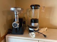 Waring Pro meat grinder, Black & Decker blender, and Oster hand mixer sitting on a side table against a wall, appearing lightly used.