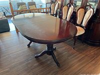 Oval dark wood dining table with pedestal base and four curved legs. Table has a visible water stain on the surface and appears heavy with a polished finish.