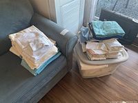 Overview of assorted bath and hand towels stacked on a gray couch and inside a plastic tote bin on the floor.