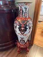 Full view of tall Asian porcelain vase on carved wood stand showing overall item and design.