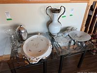 Wide view of entire lot on glass table showing vase, platter, glass bowl, urn, dessert glasses and ceramic items.