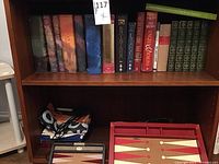 Wooden shelf holding fantasy hardcover books and two portable backgammon sets with playing pieces and dice.