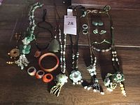 Full view of all the carved stone jewelry pieces arranged on a wooden surface, including necklaces, rings, and bracelets.