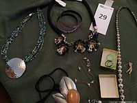 Photo of various costume jewelry pieces on green fabric background including necklaces, bracelets, rings in box, and lapel pin