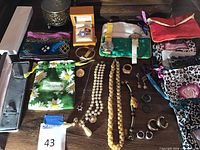 Full overview of assorted costume jewelry items including necklaces, rings, earrings, watches, scarves, jewelry bags, and boxes on wooden table