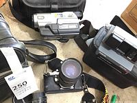 Lot with Pentax camera with attached lens, Polaroid instant camera in case, and Sony Handycam in case.