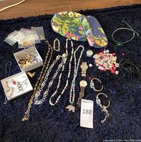 Full lot layout showing mixed jewelry including necklaces, watches, beads, and findings on dark fabric with floral pouch