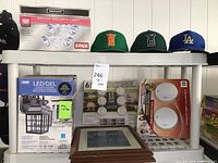 Shelf with boxed Defiant motion security lights, LED outdoor lanterns, LED puck lights with remote, smoke alarms, picture frames, and sports hats