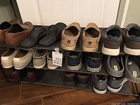 Front view of three-tier shoe rack displaying multiple pairs of men's footwear size 10.5 including shoes and slippers in various colors and brands.