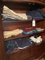 Three-tier wooden shelf with folded men's pants and shirts in tan, navy, grey, green, white and plaid