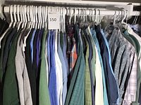 Full rack of men's large size shirts and T-shirts hanging on white plastic hangers in a closet rod. Varied colors and patterns mostly casual styles.