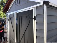 Front view of grey plastic shed showing black double doors, silver trim and roof peak