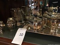 Tea service set of silver plated teapot, sugar bowl, creamer, ice bucket, and tray on reflective surface