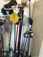 Photo showing several mops, brooms, a fruit picker, and men's black ice skate size 10.5 hanging on wall.