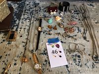 Full lot view showing watches, necklaces, bracelets, earrings, brooches, and loose items spread out on a gray blue carpet.