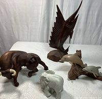 Overall view of all animal figurines including the charging bull, elephant, dolphins, and swordfish grouped on a white cloth.