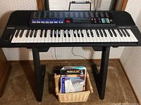 Full view of Casio CT-470 keyboard on stand with basket of manuals and sheet music below