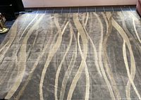 Top view of the large area rug showing the abstract wave-like cream lines over gray background.
