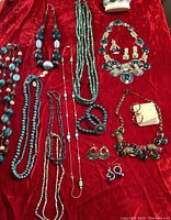 Full assortment of costume jewelry pieces including long beaded necklaces in blue shades, several pairs of earrings, bracelets, and statement necklaces with large colored stones.