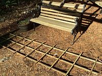 Photo showing a side view of the garden bench, planter pot in the background, and the full wooden trellis on the ground beside the bench.