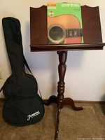 Photo showing black Jasmine guitar carrying case next to a wood music stand holding sheet music.
