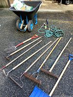 Overall view of wheelbarrow with garden tools and hoses laid out on pavement