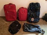 Full view of the 3 wheeled luggage and 2 duffel bags arranged on the floor, showing materials, colors and sizes for identification.