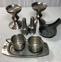 Set of two pewter candle holders with wide bases, creamer, sugar bowl on floral tray, salt and pepper shakers, and a decorative spoon ladle.