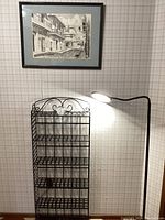 Photo showing black metal slim shelf, adjustable LED lamp, and framed monochrome art print hung on wall.