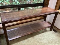 Full view of the console table showing solid wood construction, rectangular shape, and cane bottom shelf.