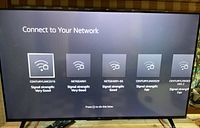 TV screen displaying 'Connect to Your Network' screen showing multiple WiFi networks available with signal strengths.