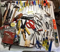 Full overview of the assortment of hand tools including hammers, screwdrivers, pliers, and measuring tools laid out on white cloth.