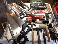 Overview photo showing multiple hand tools spread on a table, including saws, brushes, screwdrivers, wrenches, mallets, and clamps, highlighting the variety in the lot.