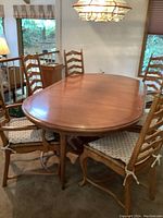 Oval wood dining table with six chairs arranged around it, showing the full table and chairs with cushions