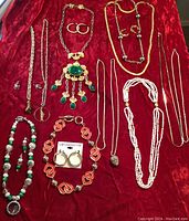 Full overview of all vintage costume jewelry laid out on red fabric background, showing variety of necklaces and earrings.